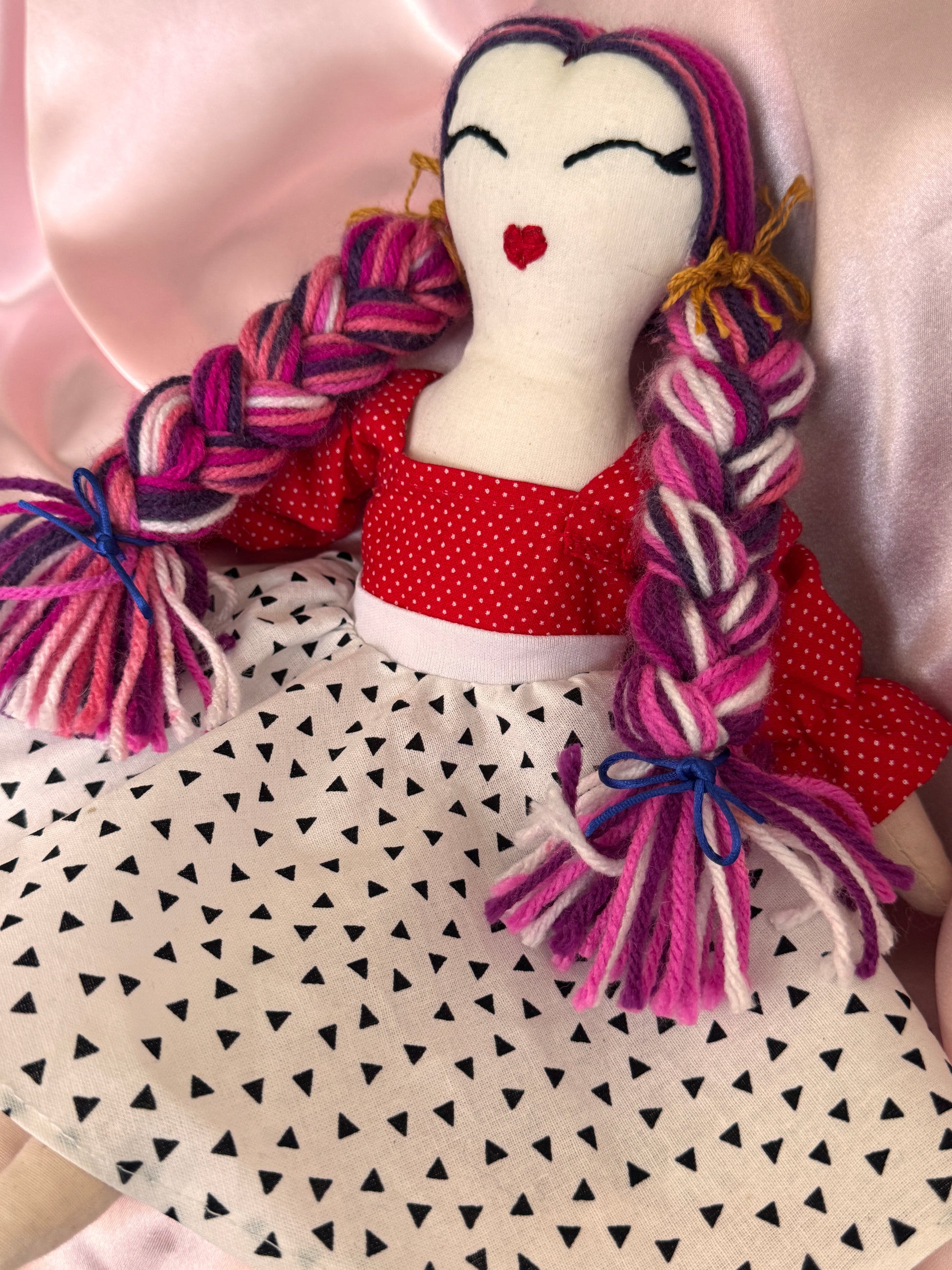 Stuffed toy with braided hair and a red bow on a patterned surface